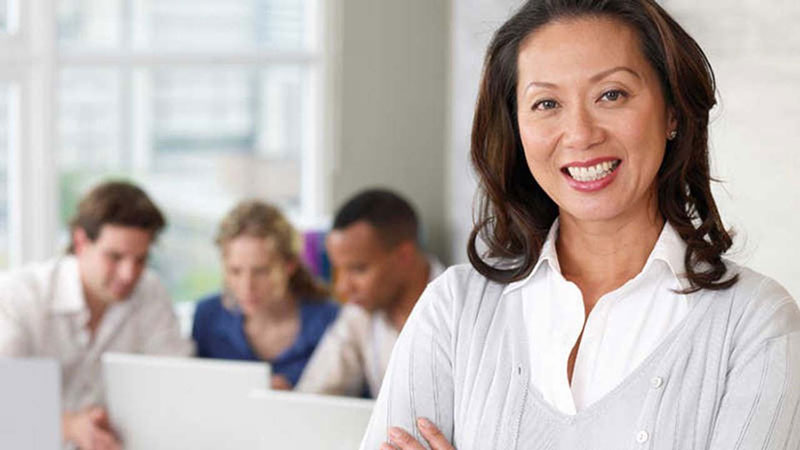 Closeup of a woman smiling with three people on their laptops in the background.