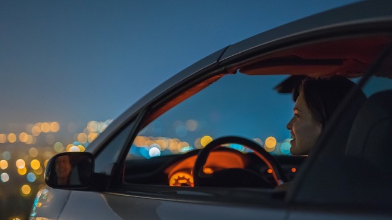 A young woman sitting in a car in the evening