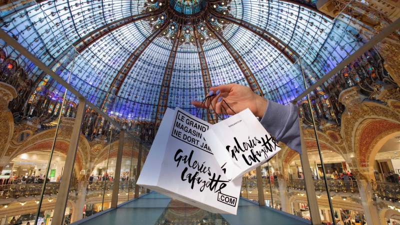 Hand holding Galeries Lafayette shopping bags inside the iconic Paris department store
