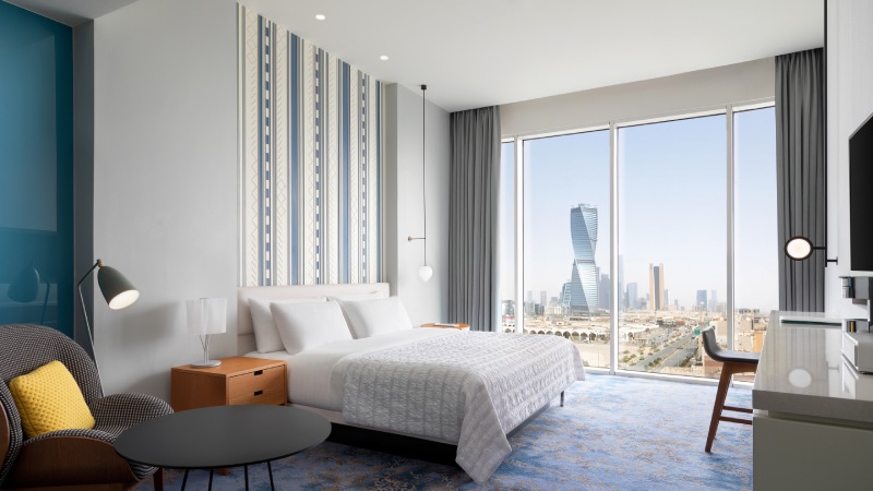Modern Marriott hotel room with king-size bed and city skyline view through floor-to-ceiling windows.
